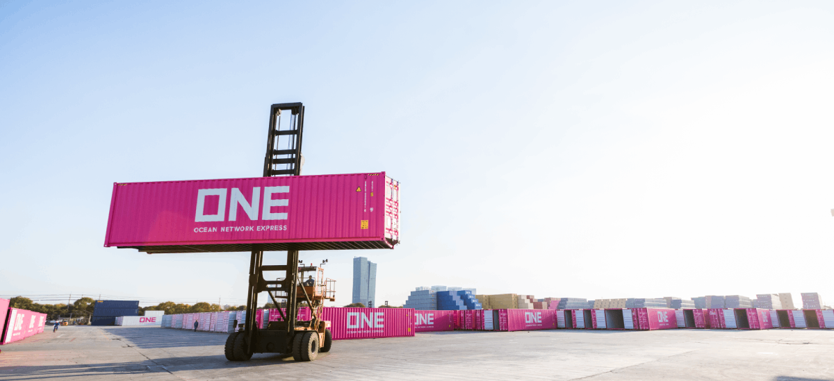 A container handler lifts a magenta Ocean Network Express (ONE) shipping container in a terminal yard